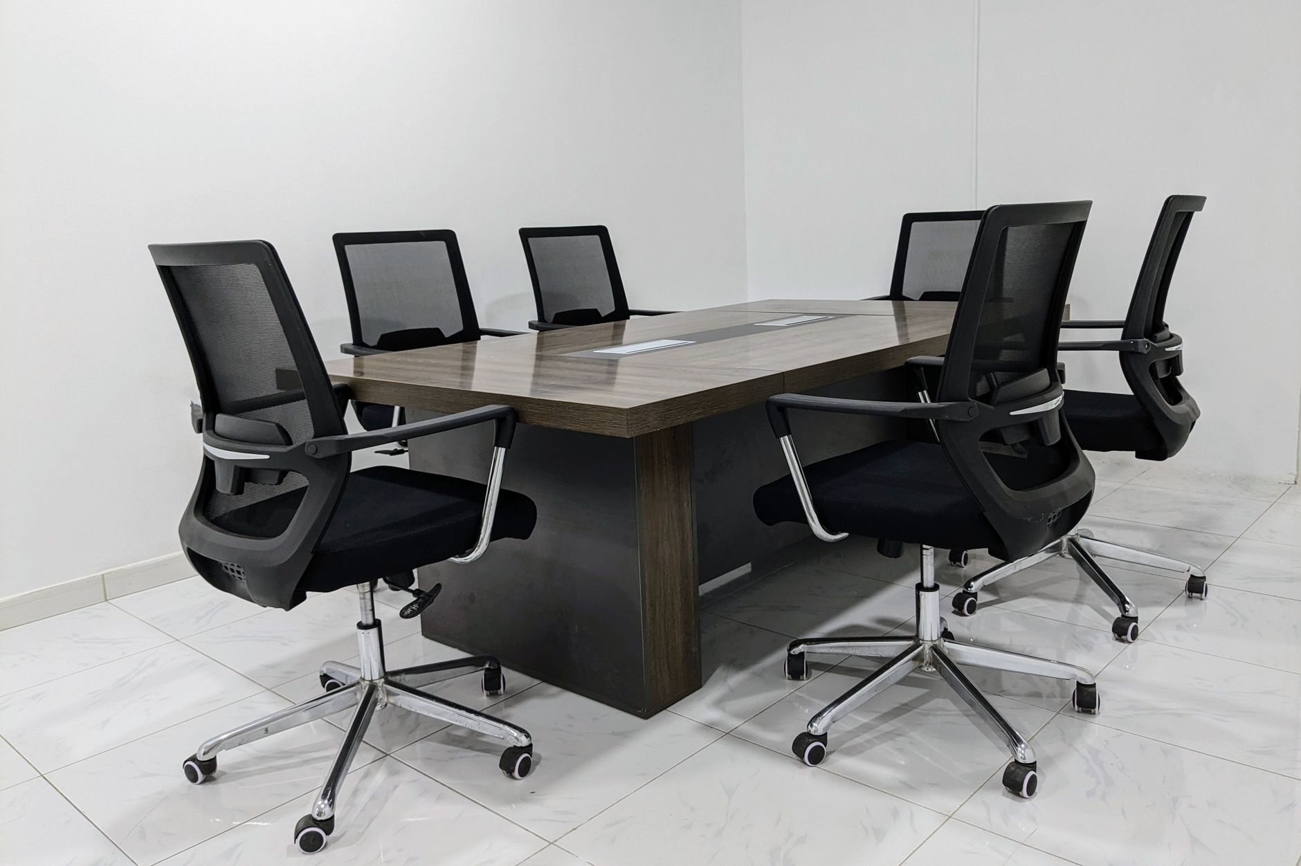 A neat and minimalistic conference room setup with black mesh chairs around a dark wooden table.