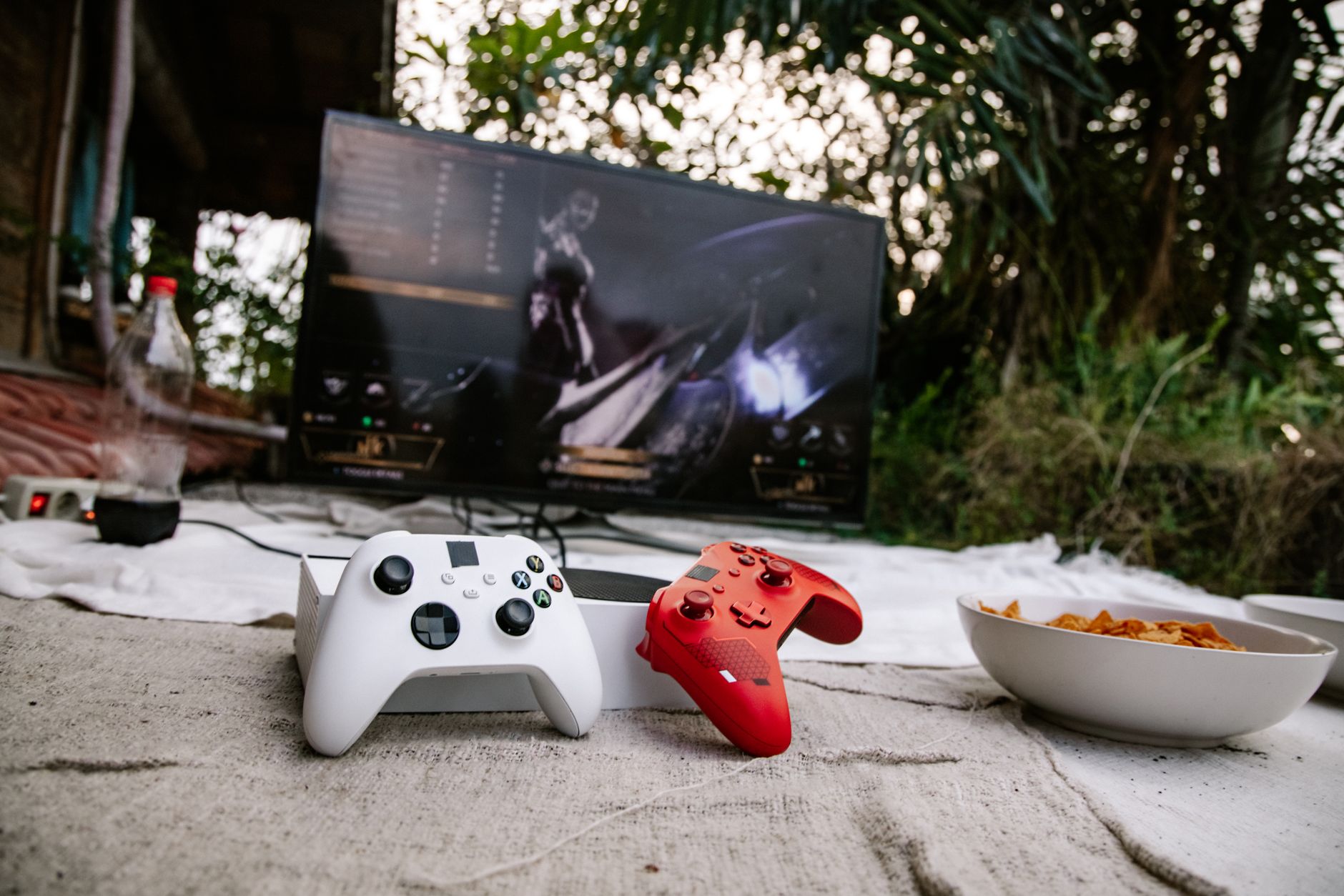 Outdoor gaming scene with controllers on a mat and a screen showing a video game.