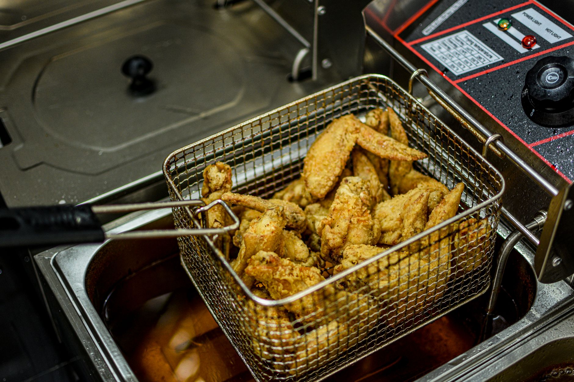 Golden brown chicken wings freshly fried in a commercial deep fryer.