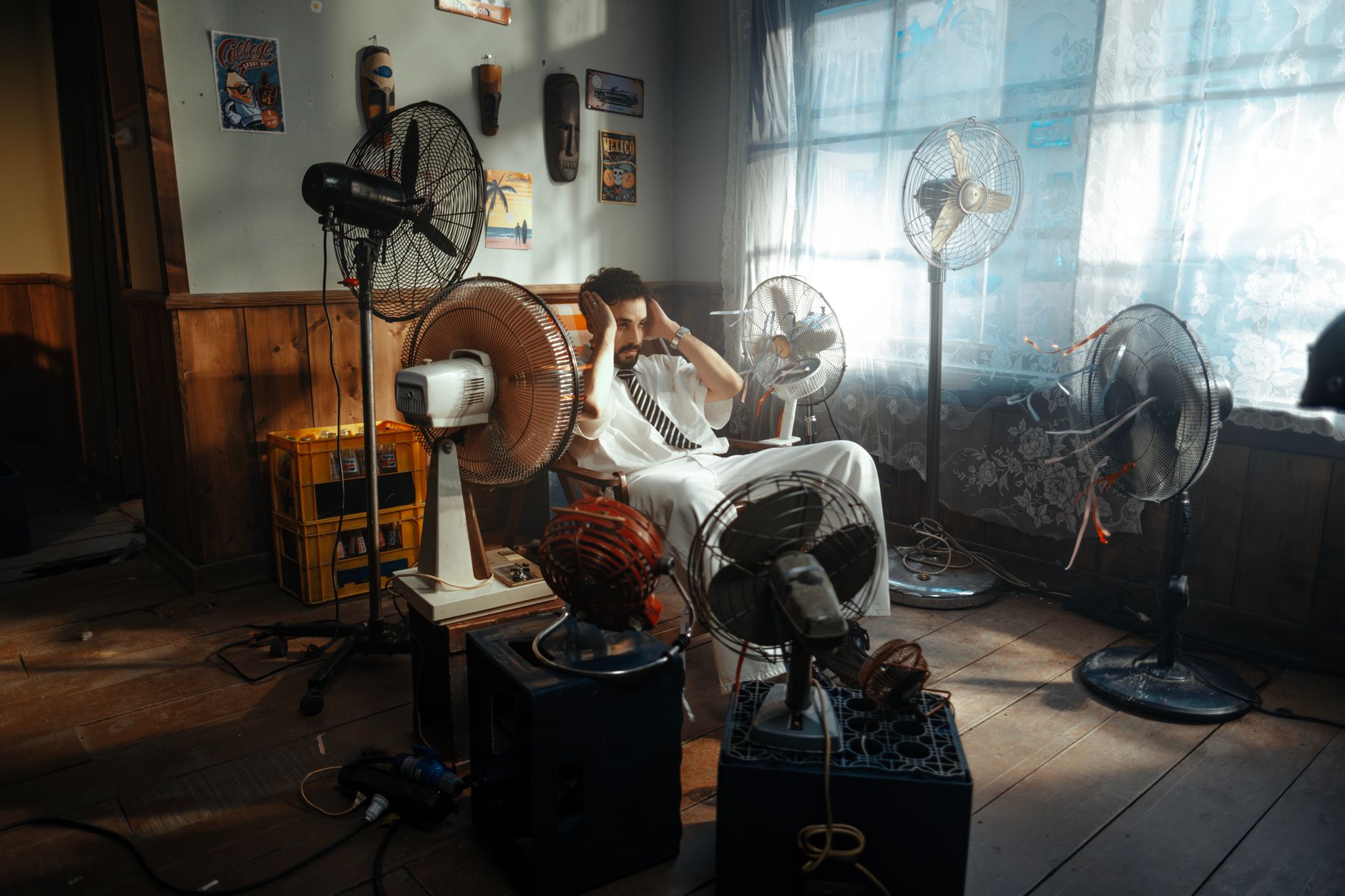 Man in white outfit sitting surrounded by several fans indoors during daytime.
