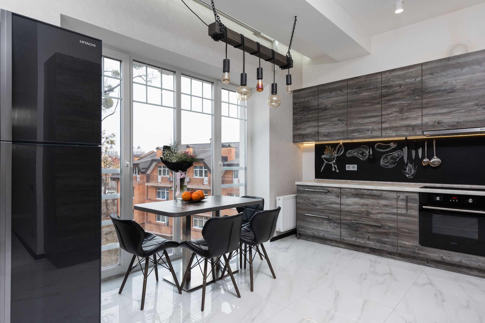 Fridge and table with chairs placed near window in stylish light kitchen with cupboards and modern kitchenware in spacious apartment