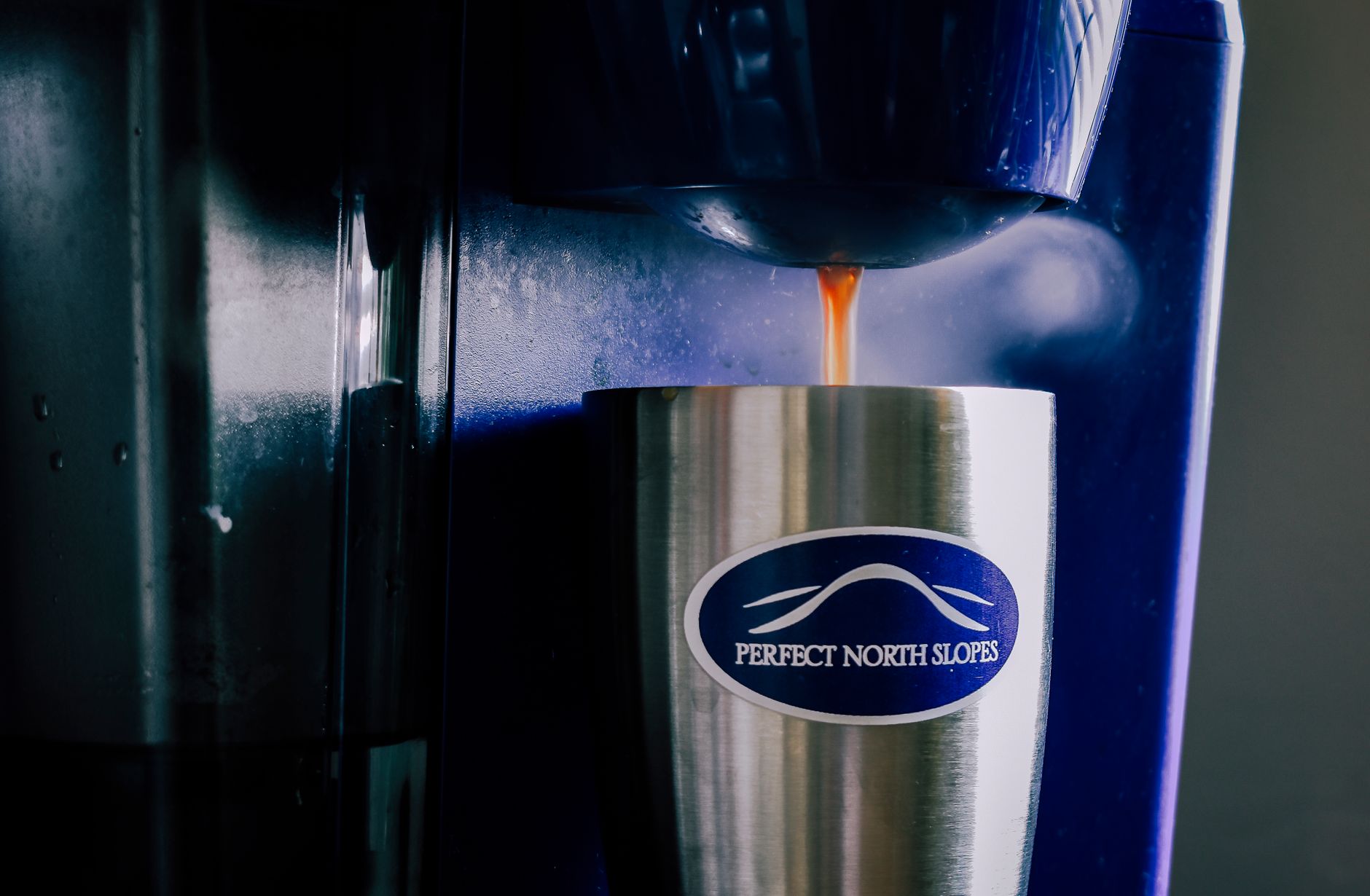 Stainless steel cup with coffee pouring from a coffee machine indoors.
