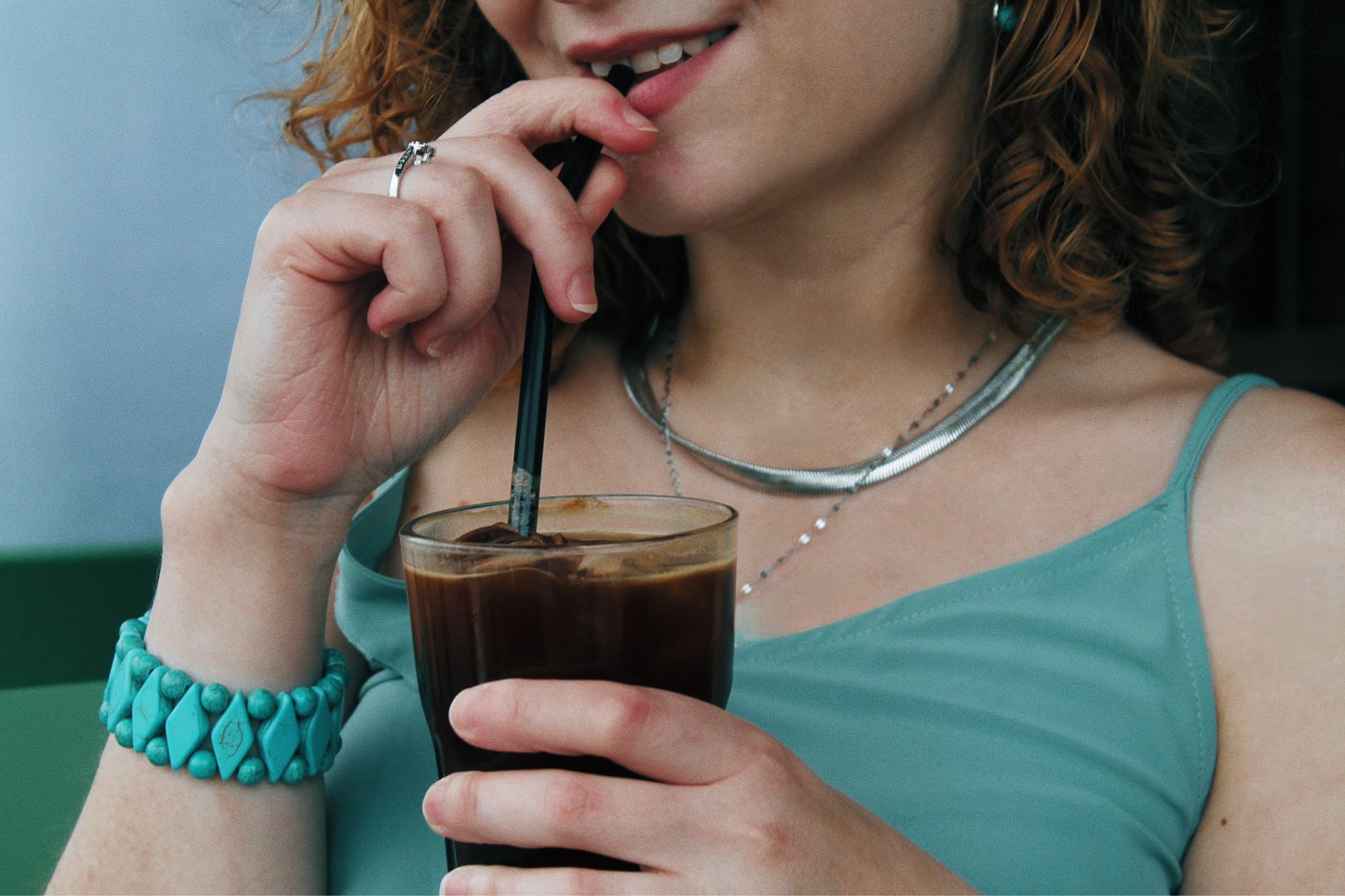 Close-up of a woman sipping iced coffee, wearing silver jewelry and turquoise bracelet.