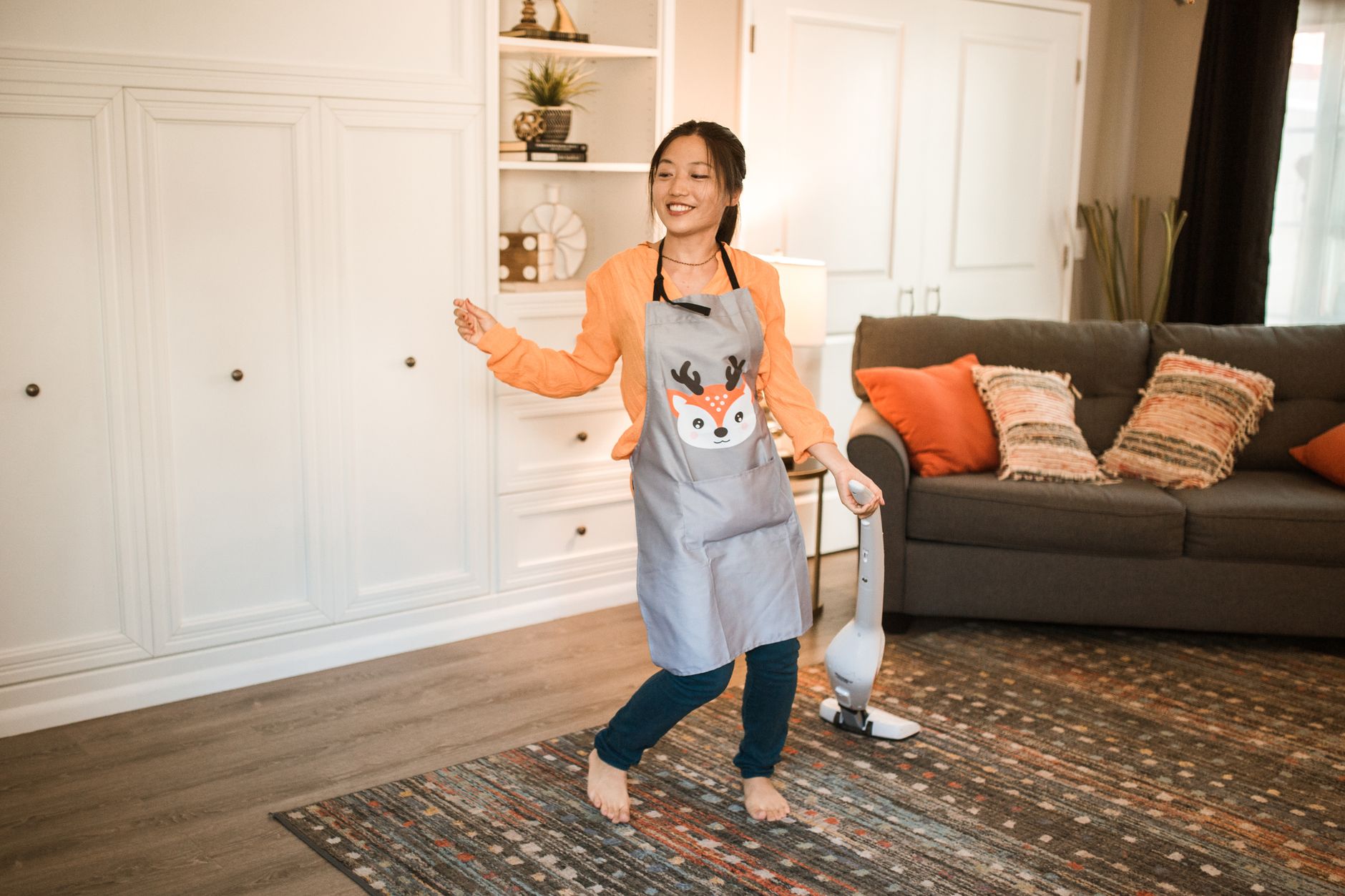 Asian woman happily cleaning her living room with a vacuum. Bright, cheerful indoor setting.