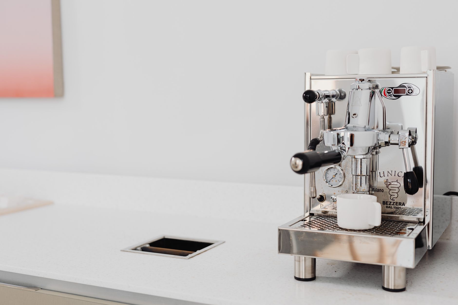 Sleek stainless steel espresso machine with cups in a bright kitchen setting.