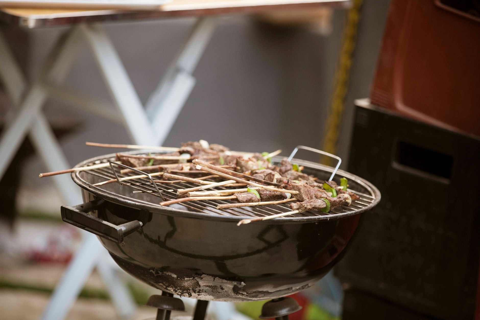 Black barbecue grill with skewered meat cooking outdoors, perfect for summer gatherings.