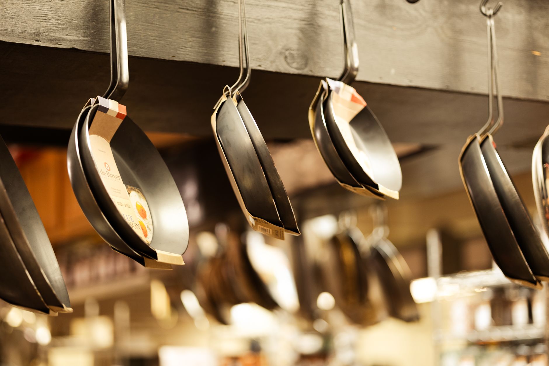 A selection of frying pans hanging in a kitchenware shop for sale.