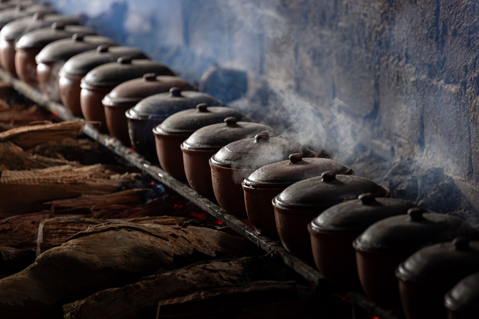 Row of steaming clay pots over firewood, showcasing authentic Vietnamese cooking.