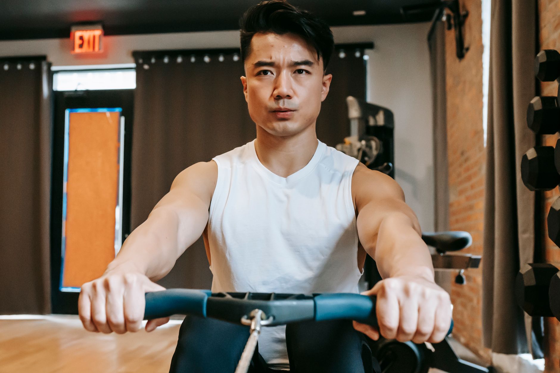 Young ethnic concentrated fit male training with rowing machine in modern sport club