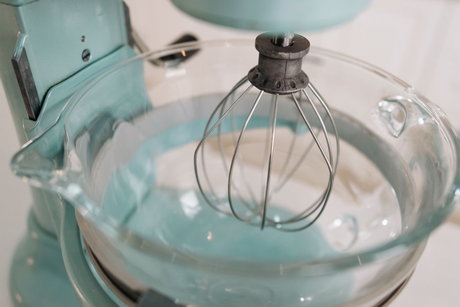 Detailed shot of a turquoise stand mixer with a whisk attachment and glass bowl, ideal for baking.
