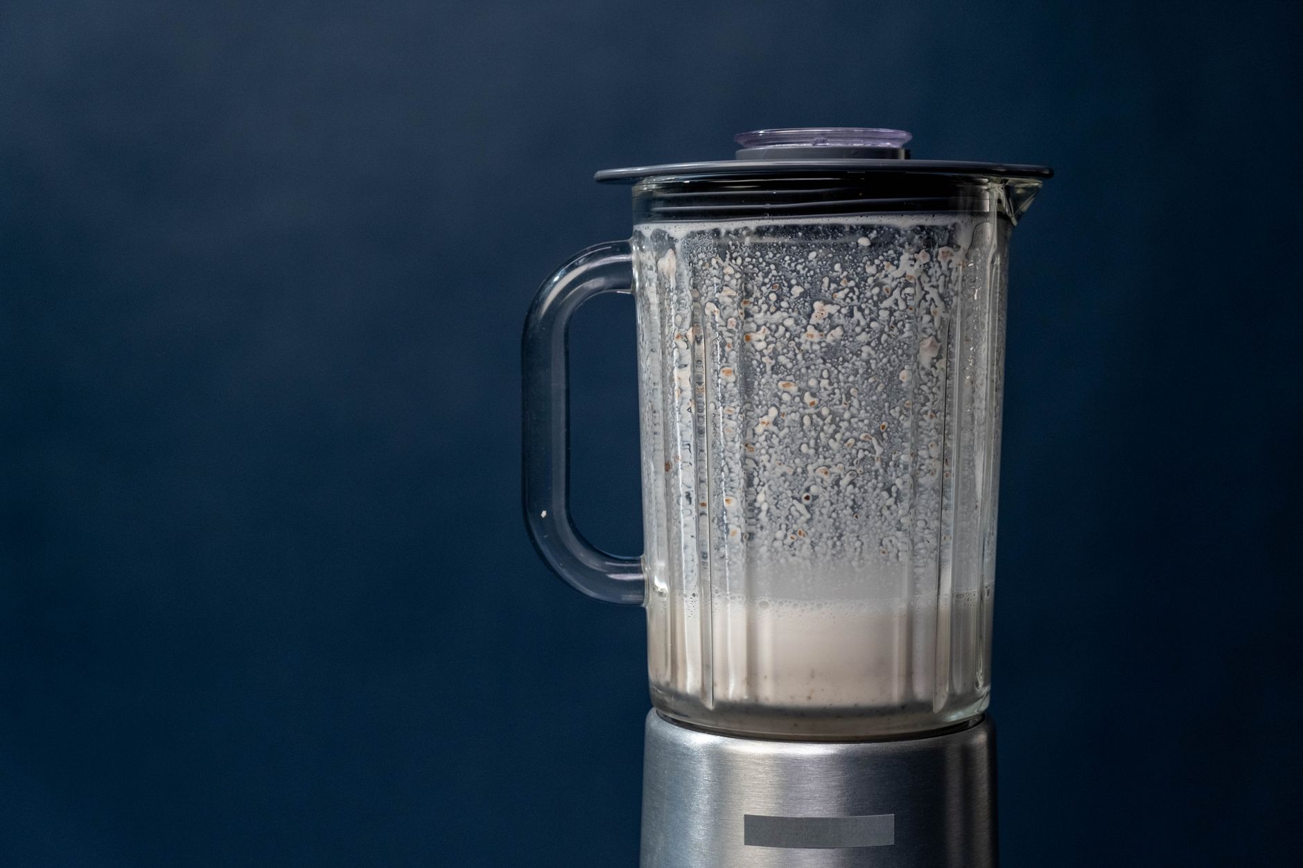 Close-up of a silver blender making a milkshake against a blue background, studio shot.