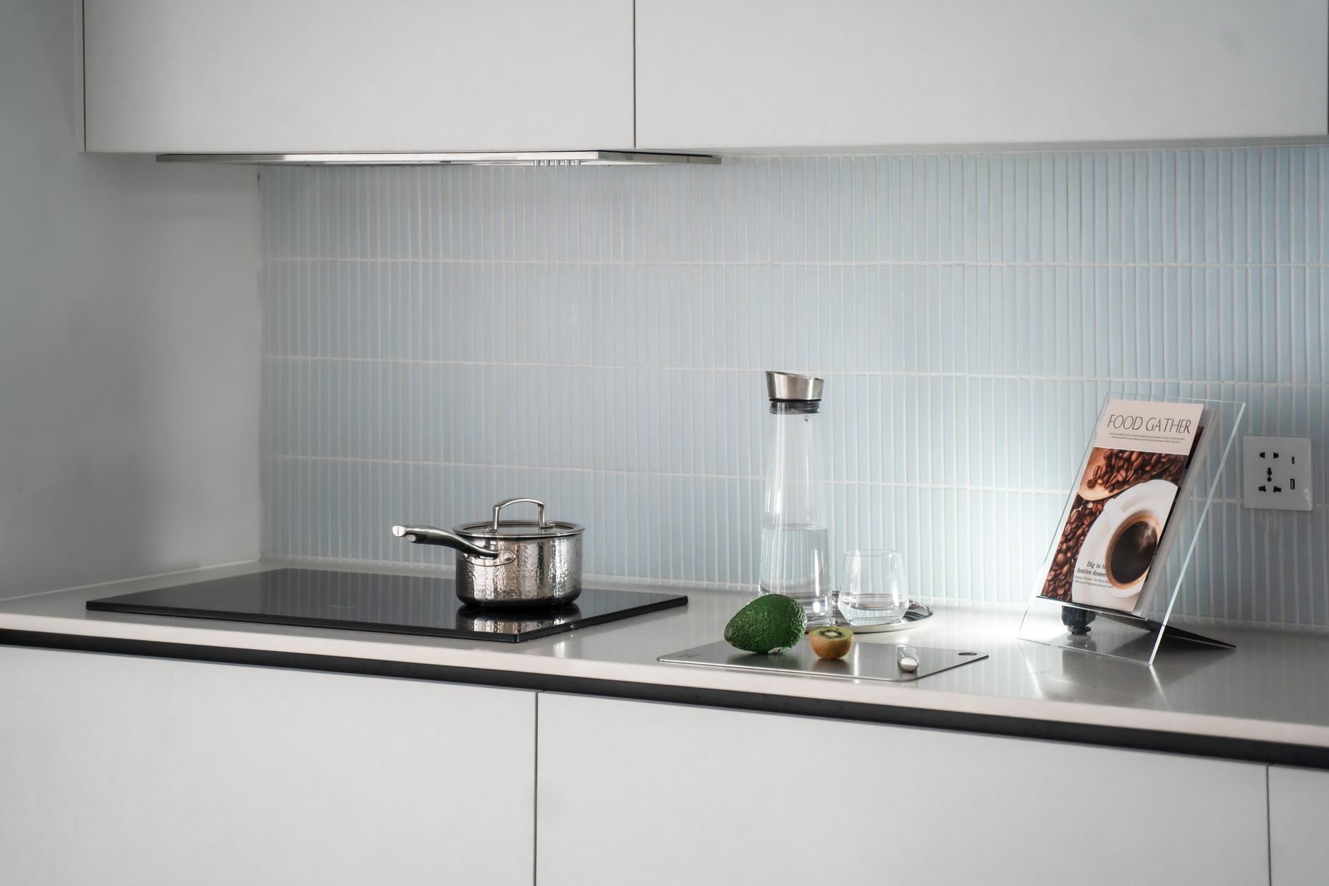 Elegant minimalist kitchen counter with induction stove, pot, glassware, and cookbook.