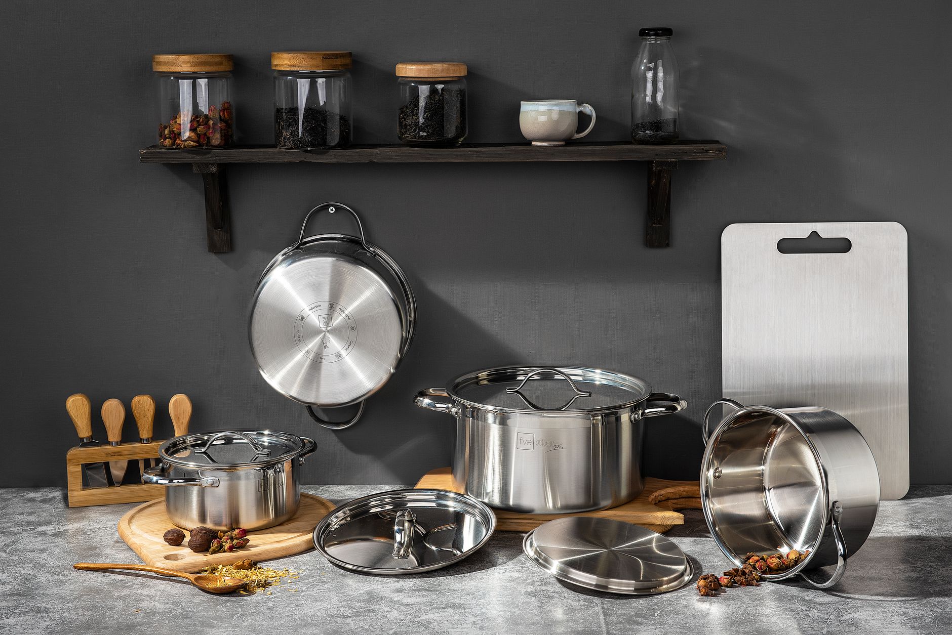 Stainless steel pots and kitchen essentials on concrete surface under shelf with jars.