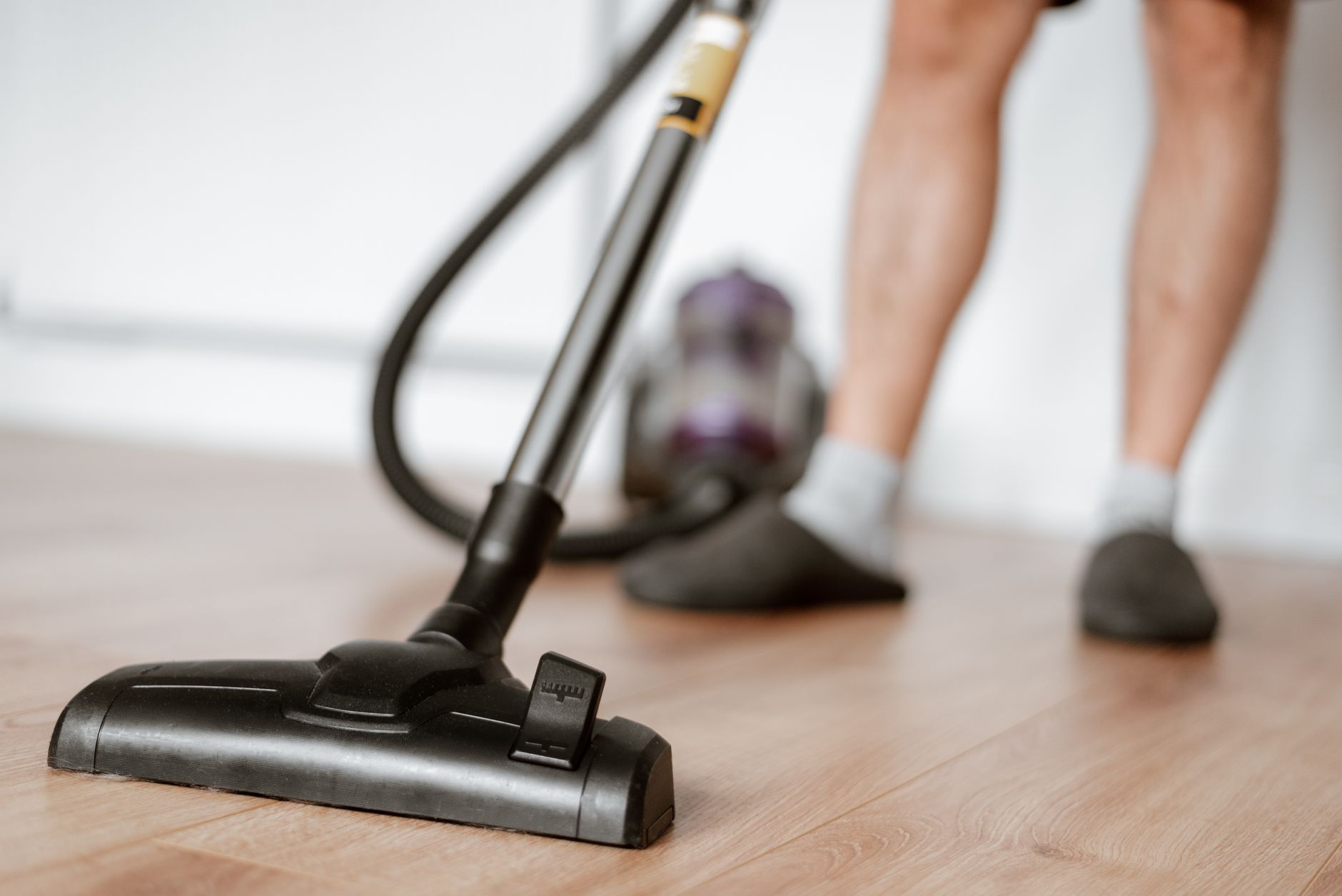 Crop anonymous male in slippers washing floor with vacuum cleaner in flat during household routine