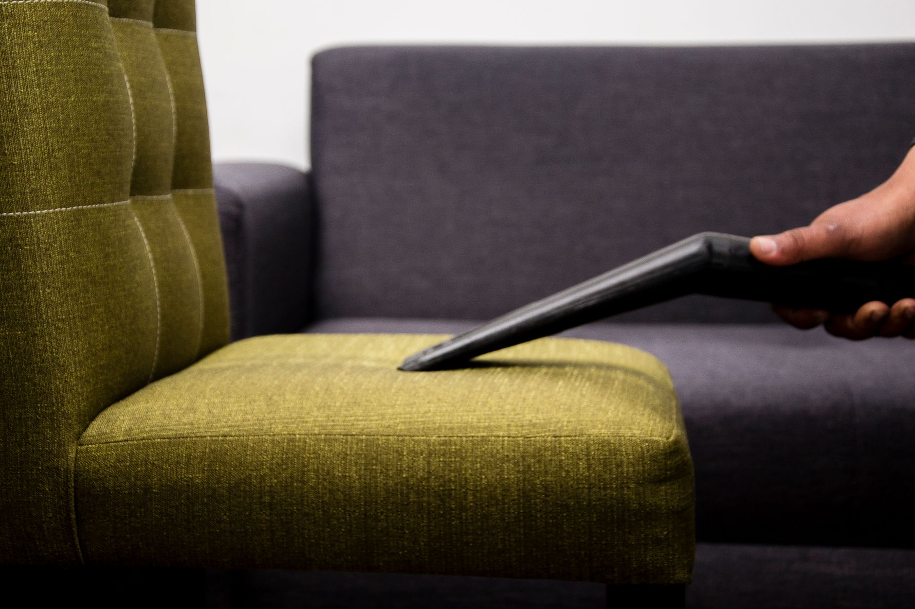 Close-up of a person vacuuming a modern sofa chair indoors, highlighting cleaning service.