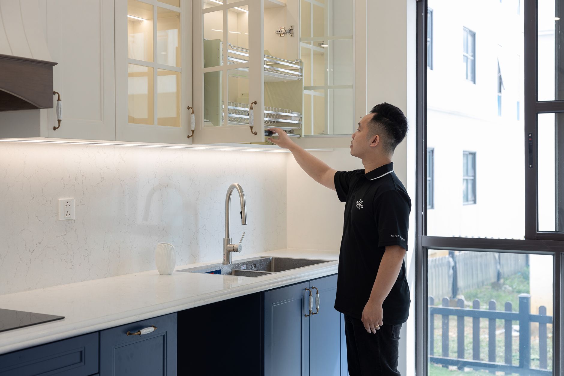 A person organizing a modern kitchen cabinet with elegant design and bright lighting.