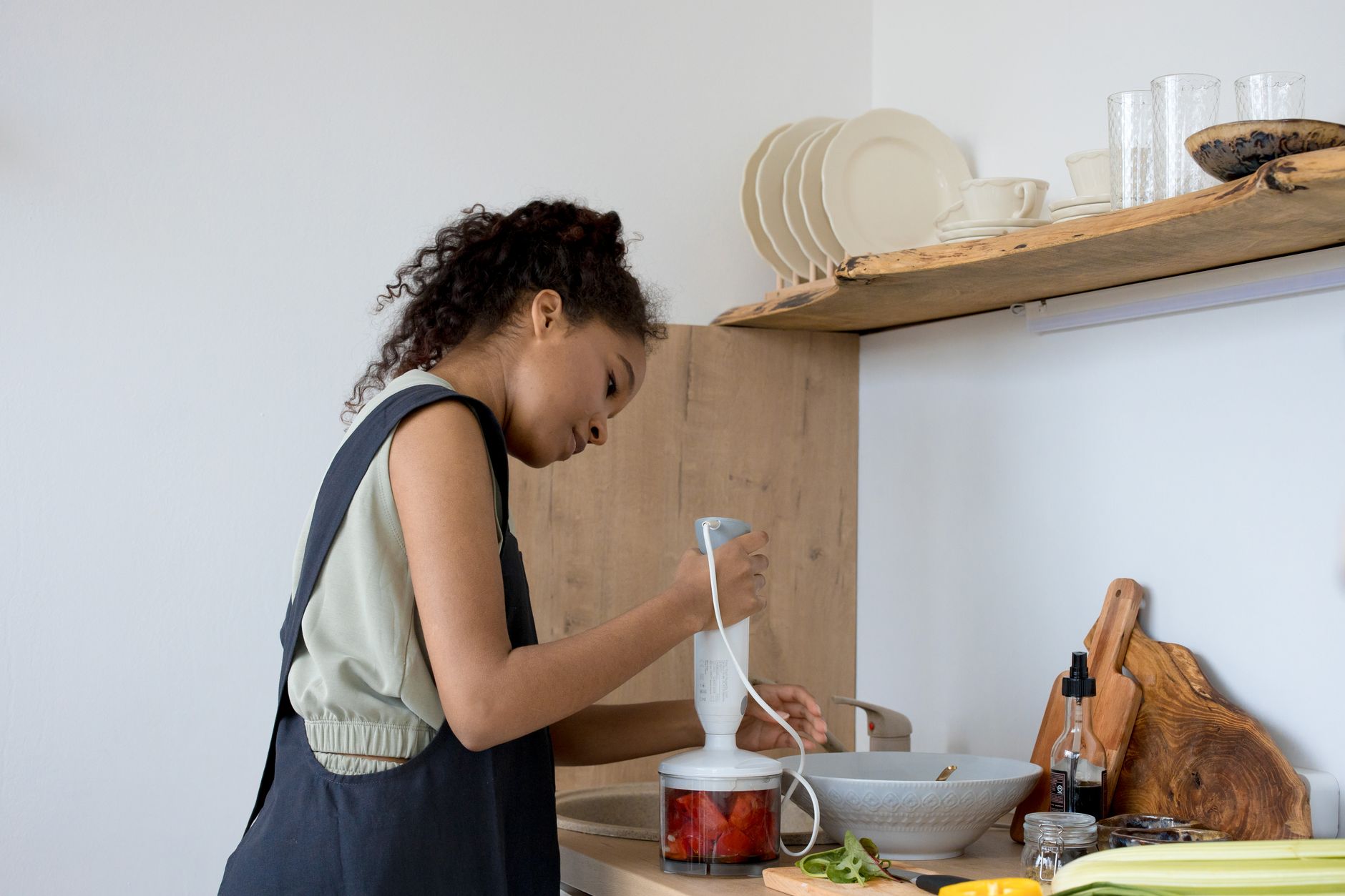 Young woman blending ingredients in a modern kitchen environment, focusing on healthy food preparation.
