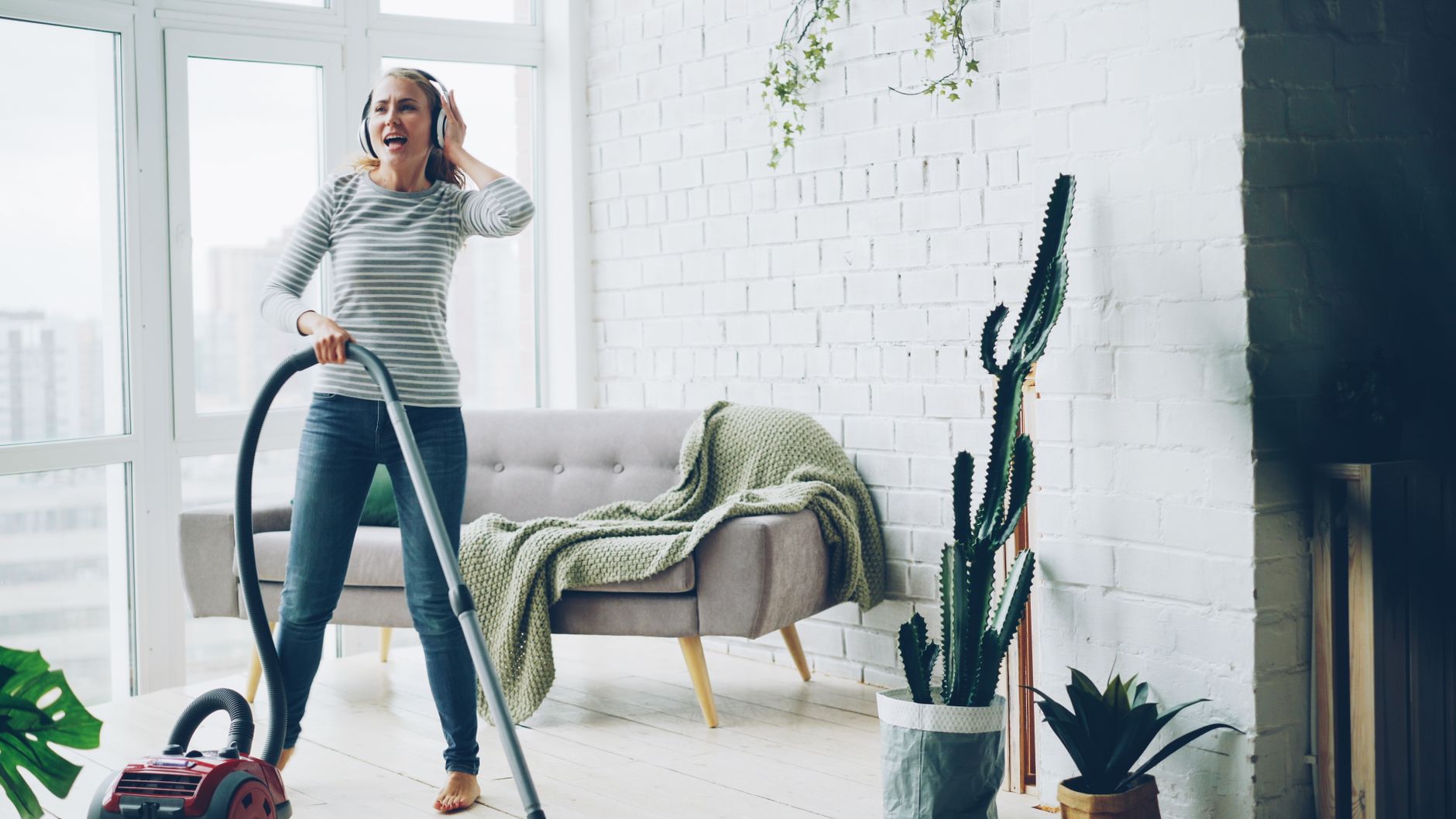 Cheerful woman vacuuming indoors while listening to music.