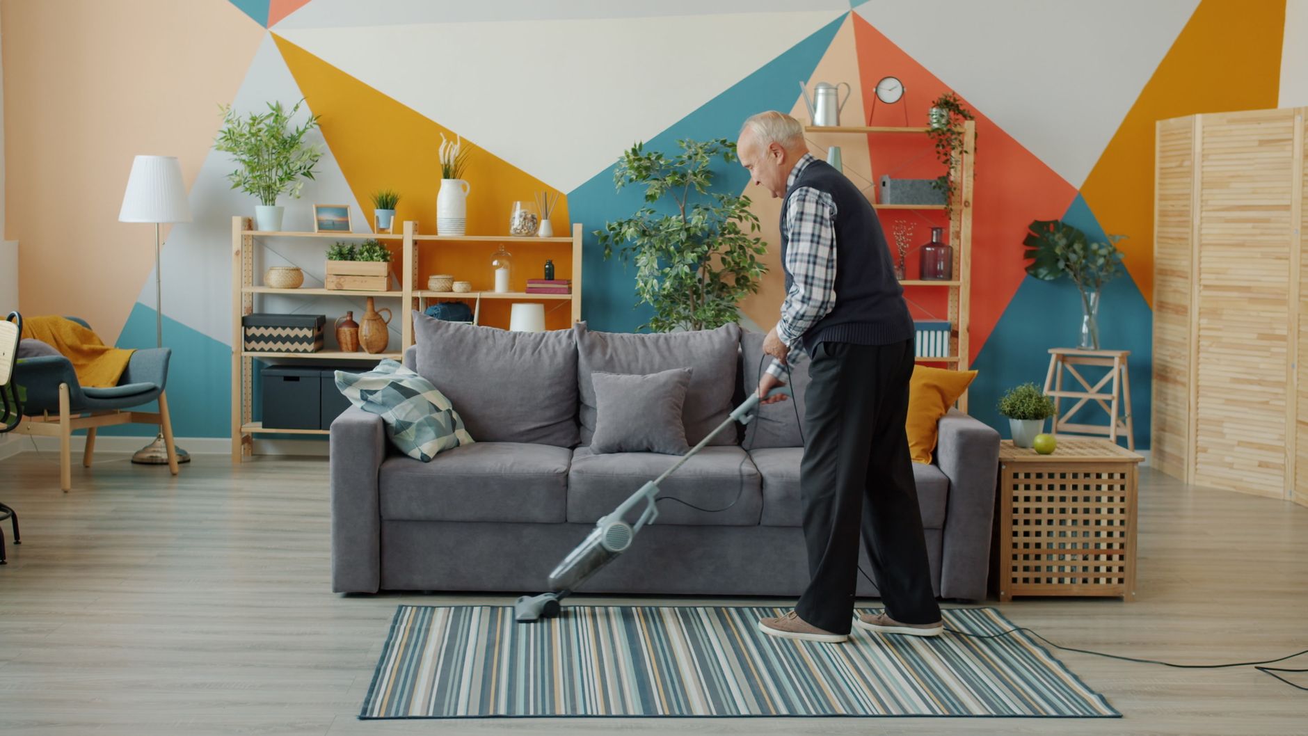 Senior man cleaning with a vacuum in a contemporary colorful living room setting.