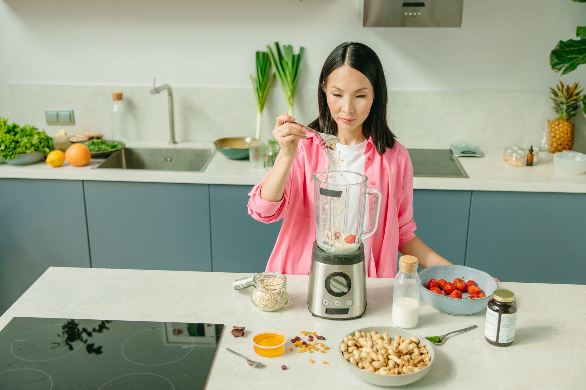 A woman in a kitchen preparing a nutritious smoothie with fresh ingredients.