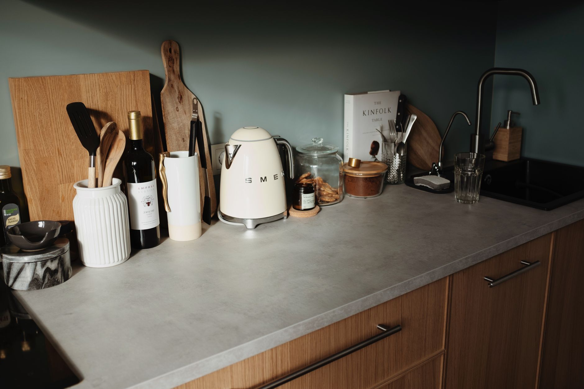 A modern kitchen counter with a Smeg kettle, wine, utensils, and wooden decor elements.