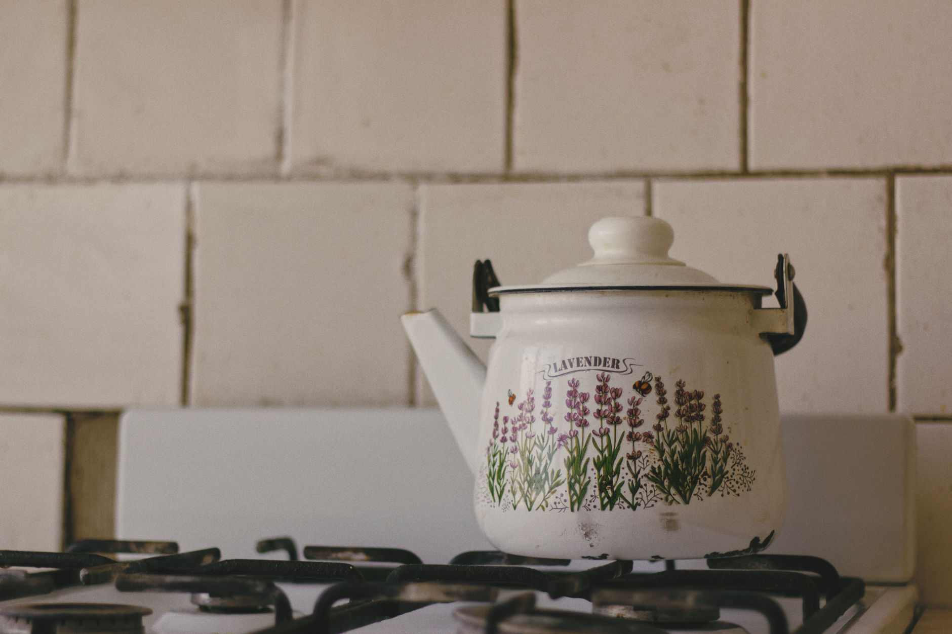 A vintage enamel teapot with lavender design placed on a kitchen stove, perfect for rustic decor themes.