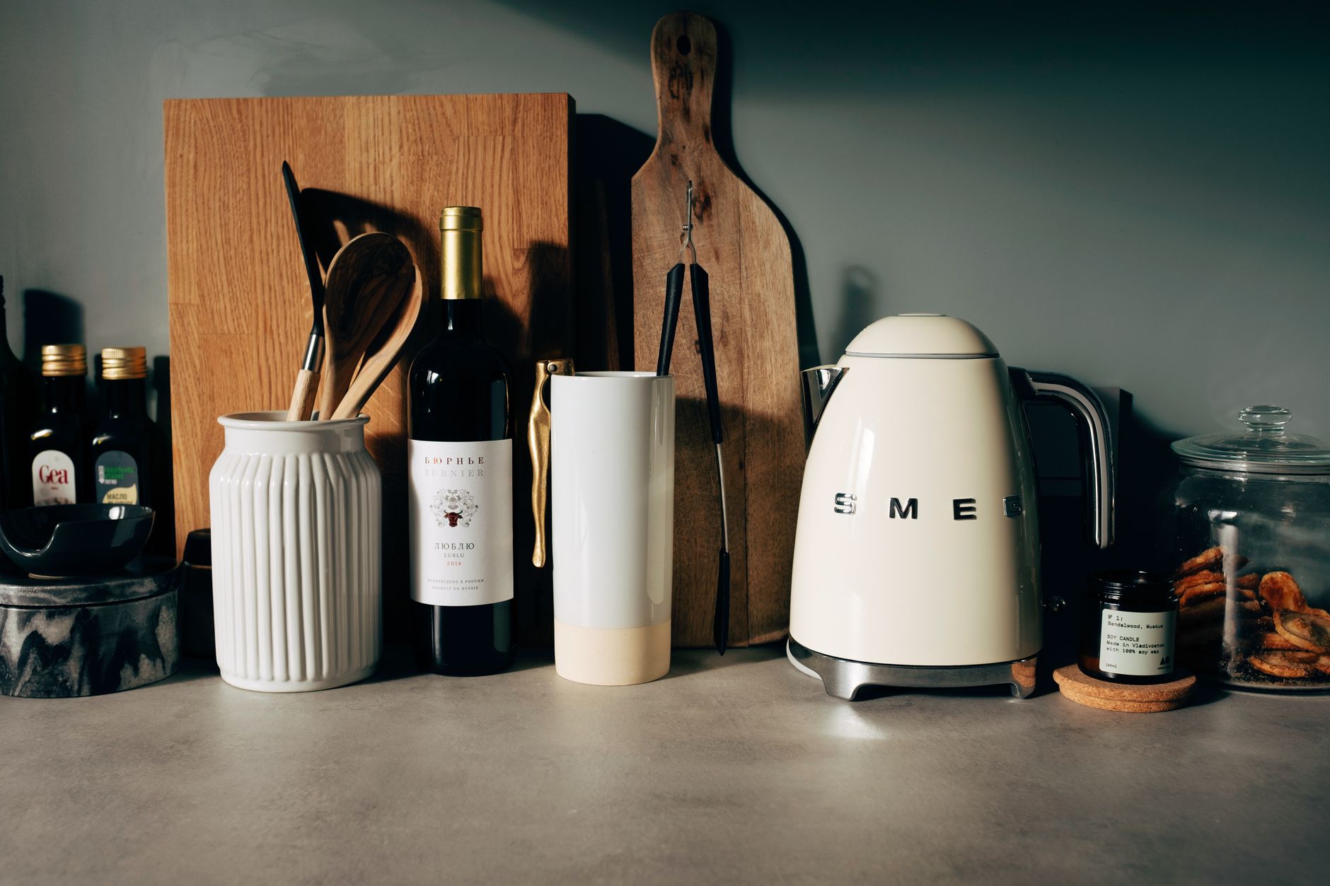 White gloss electric kettle standing next to other kitchen utensils with bottle of wine and various bowls on countertop in modern home kitch