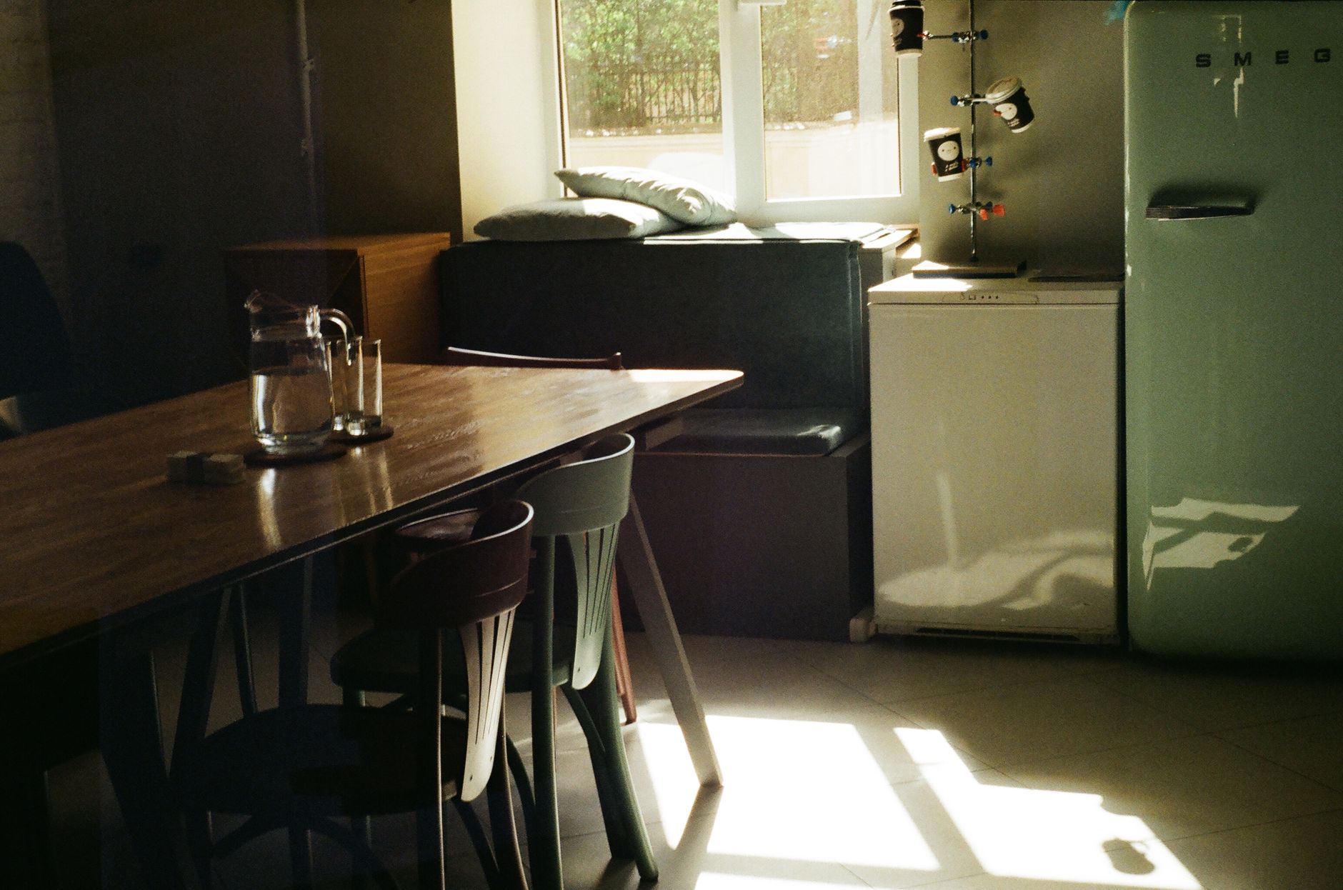 A cozy kitchen with a vintage Smeg fridge and wooden table basking in sunlight.
