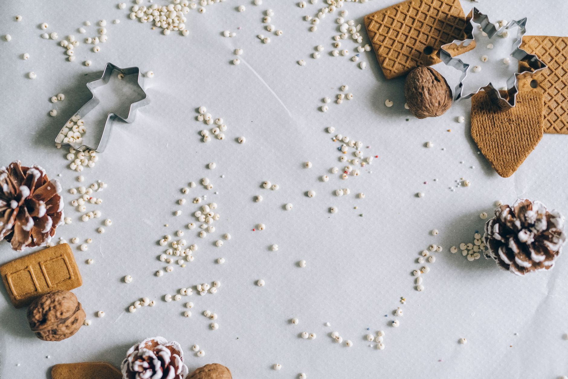 A holiday-themed flat lay with cookie cutters, nuts, and pine cones on a white surface.
