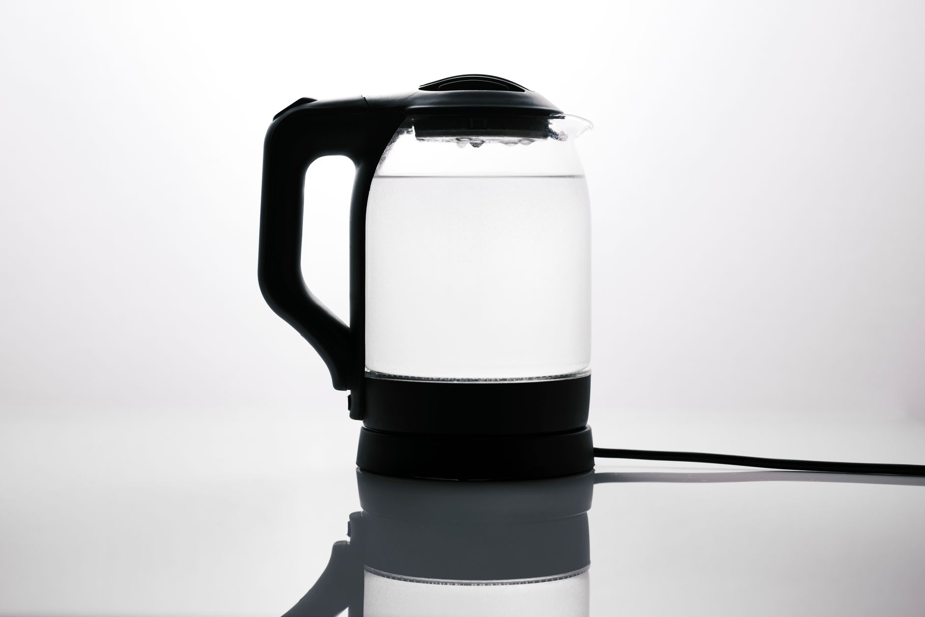 Sleek glass electric kettle with water, reflecting on a glossy surface, ideal for modern kitchens.
