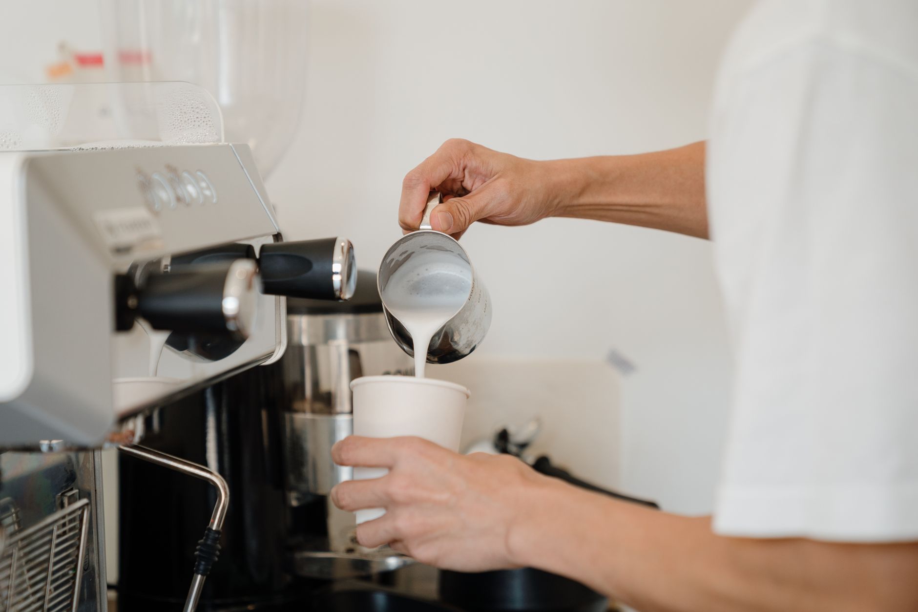 Barista carefully pouring steamed milk into a cup to create a delicious coffee beverage at a café.