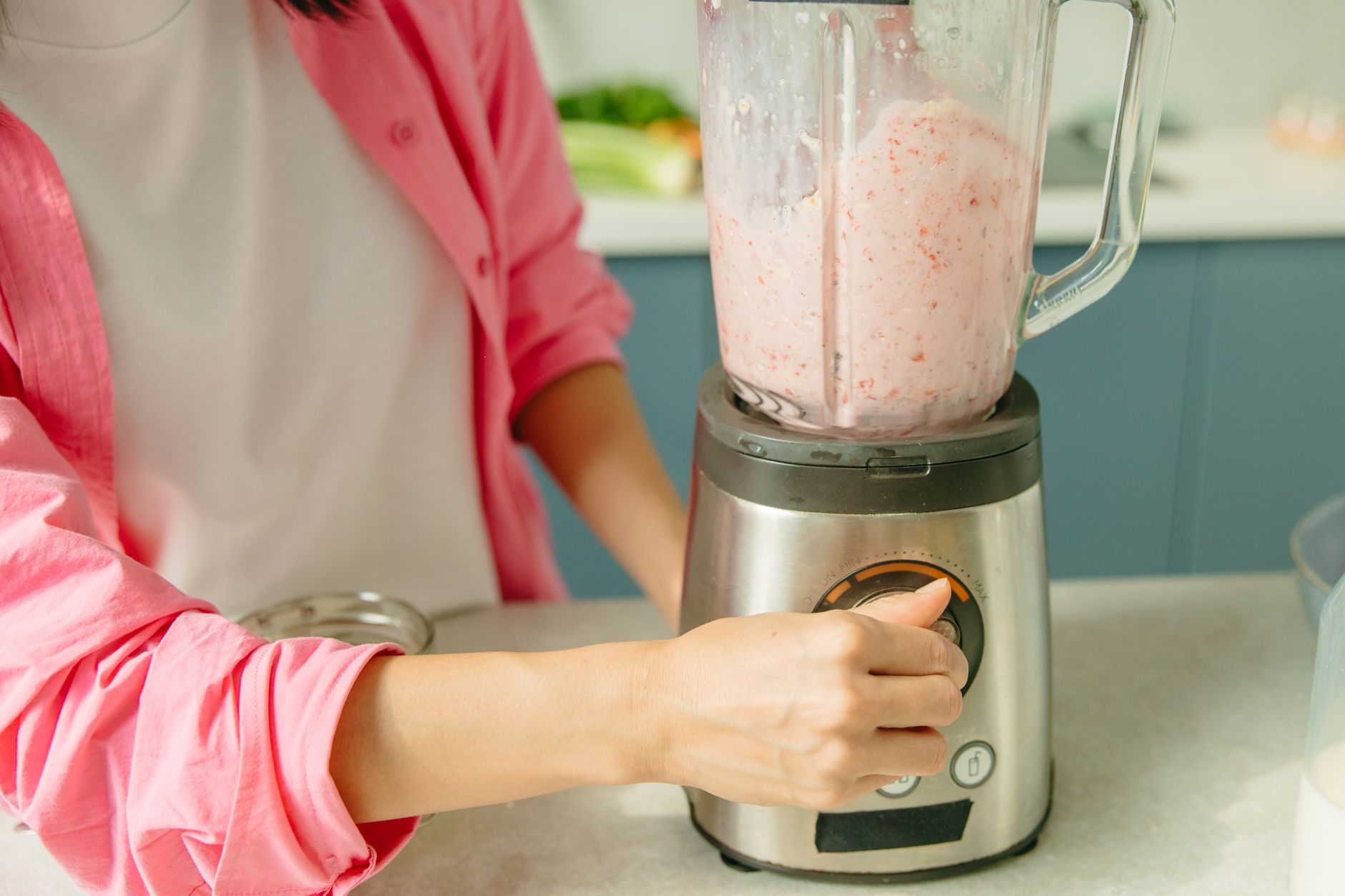 A person in pink attire using a blender to prepare a fresh fruit smoothie.