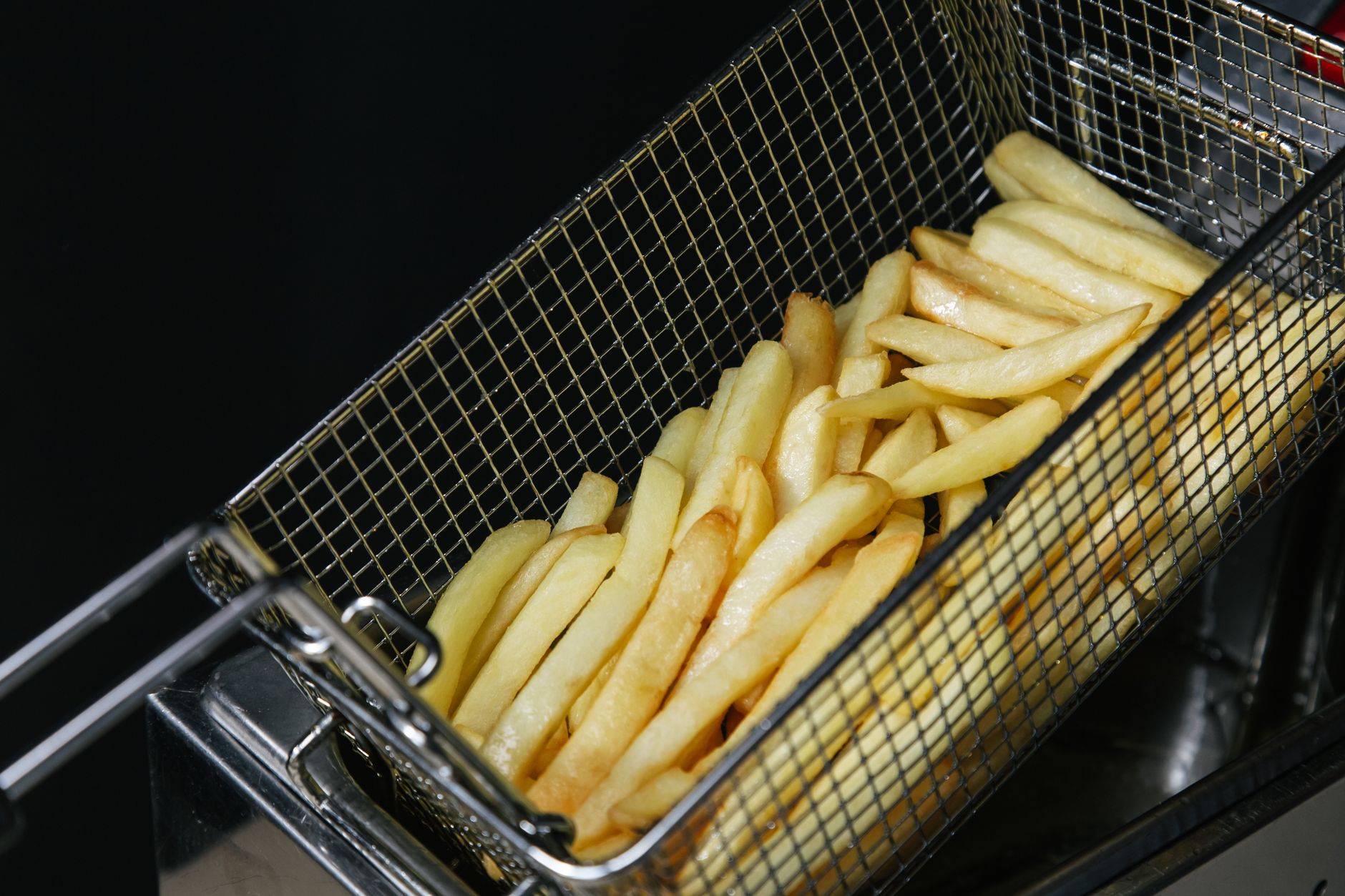 Close-up of freshly fried crispy French fries in a metal basket, highlighting fast food textures.