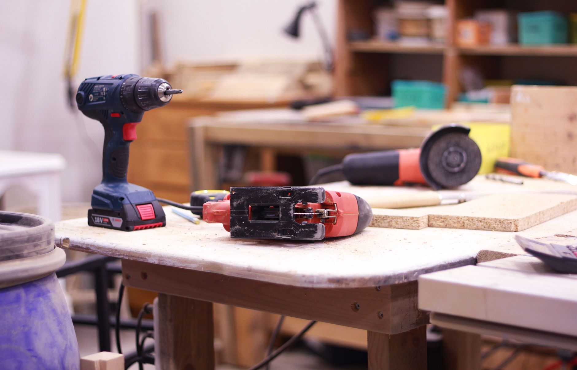 Close-up of power tools on a workshop table with a blurred background, showcasing a woodwork workspace.