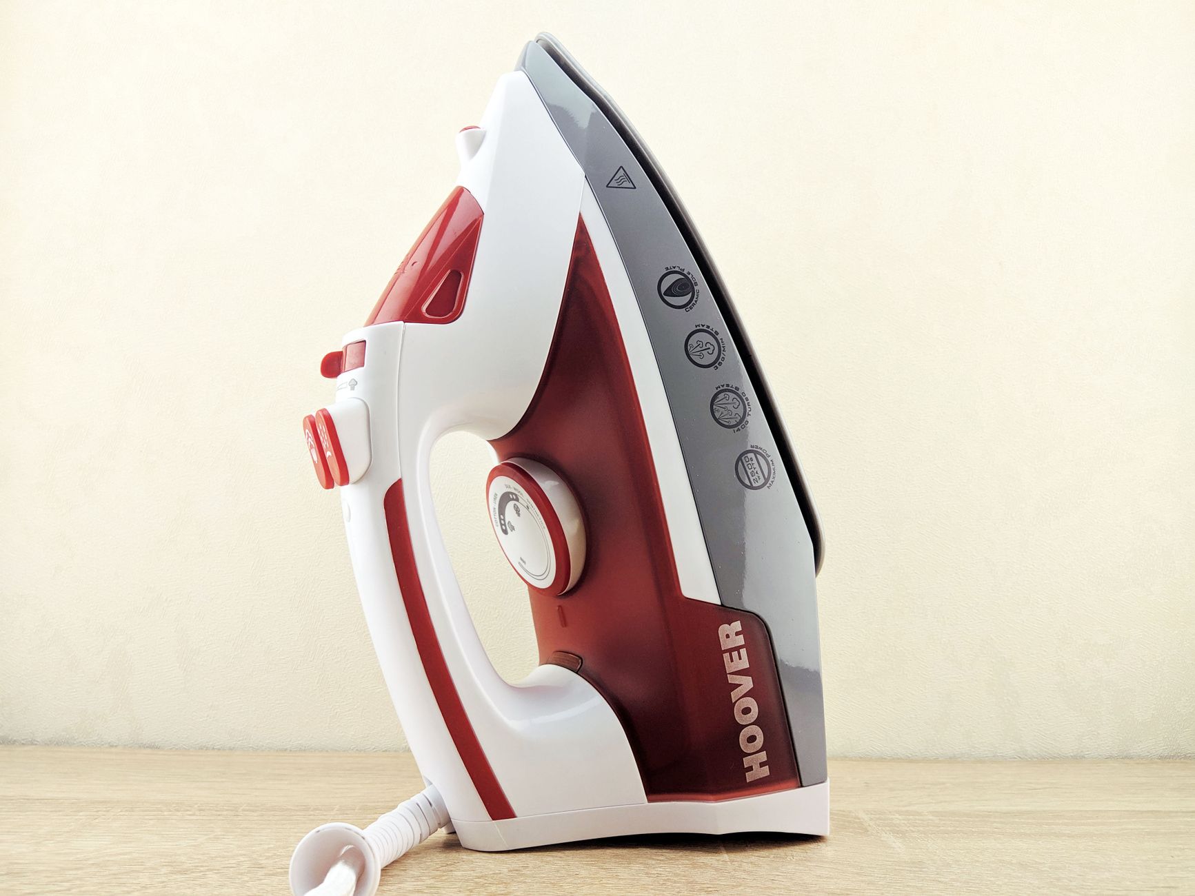 Contemporary multi functional wired iron of white and red colors placed on heel rest on white surface