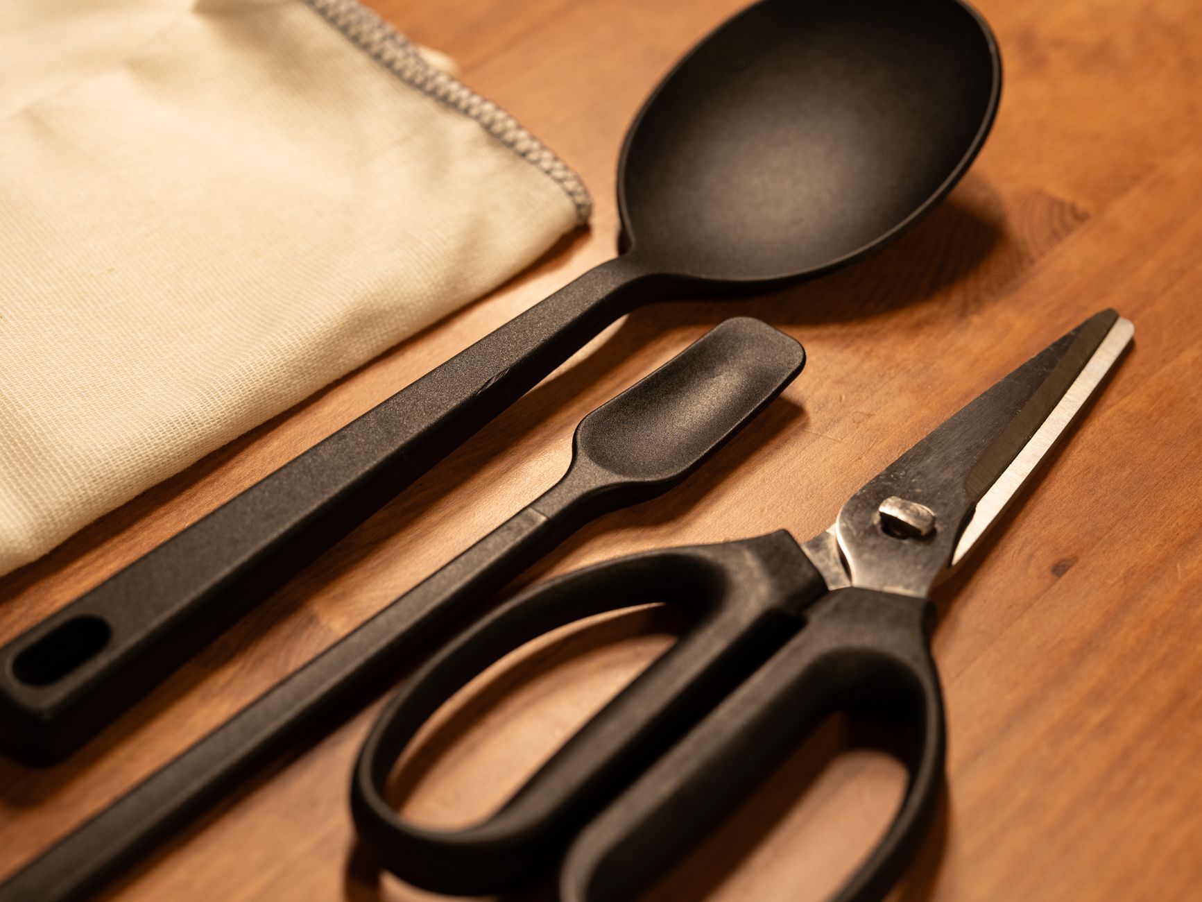 A set of modern black kitchen utensils including scissors on a wooden surface, offering a sleek culinary style.