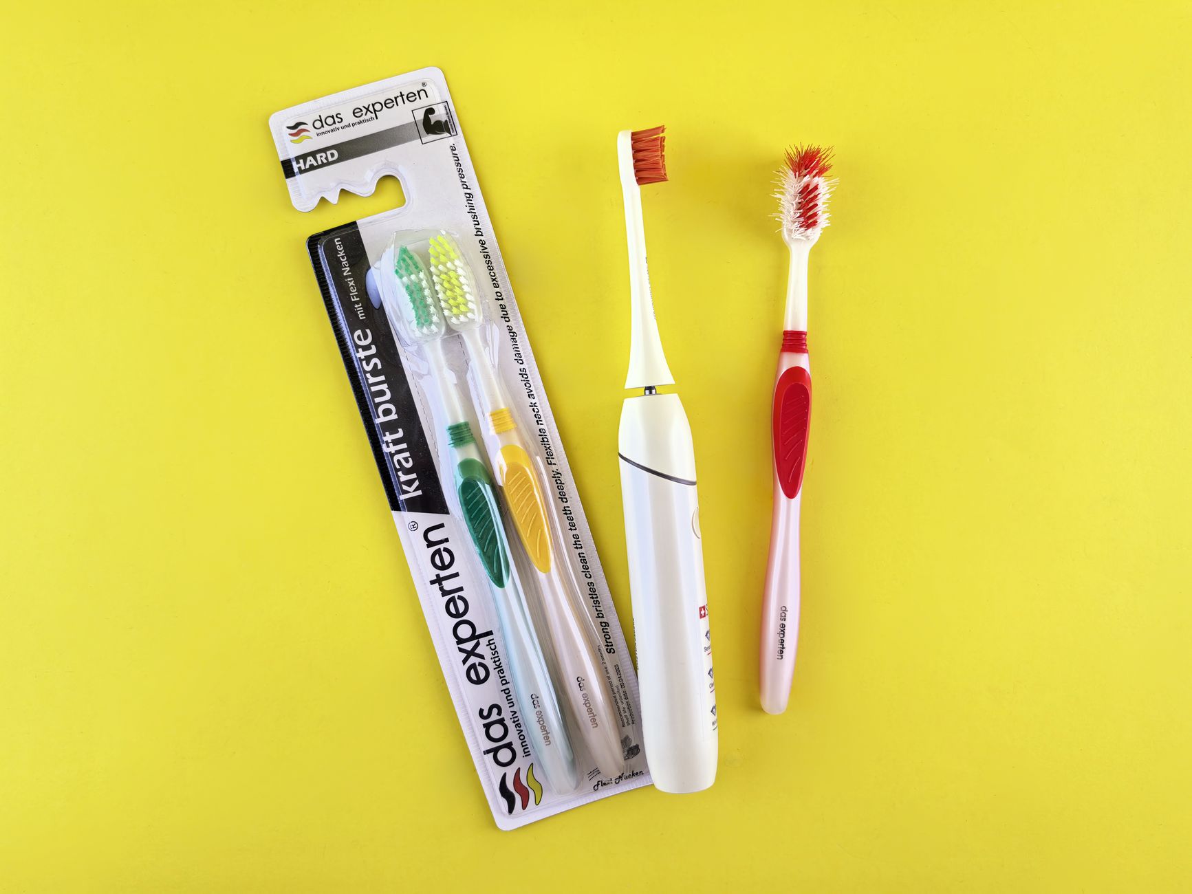 Flat lay of manual and electric toothbrushes with vibrant yellow background.