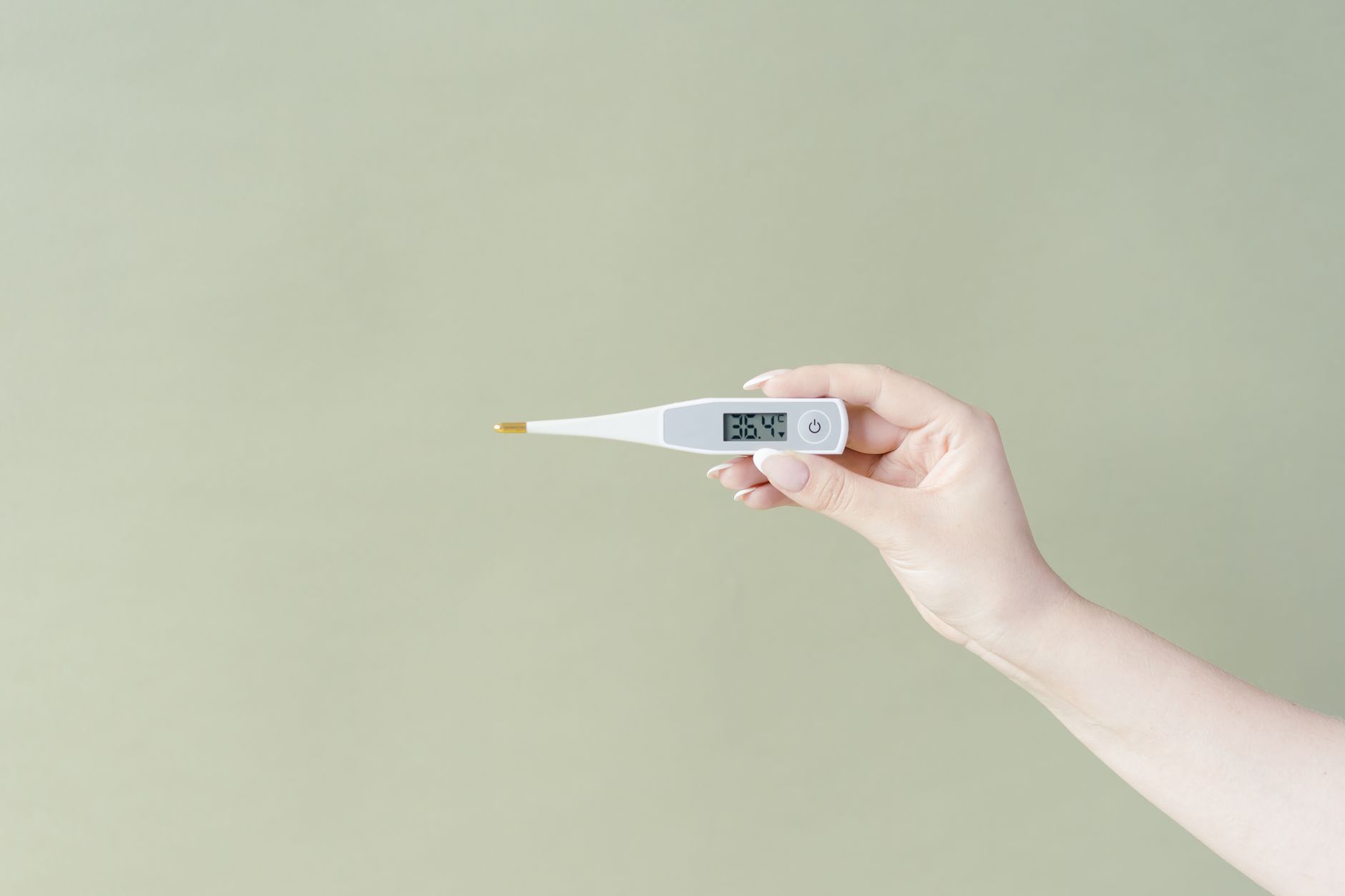 Hand holding a digital thermometer displaying 36.4°C on a light green background, minimalistic style.