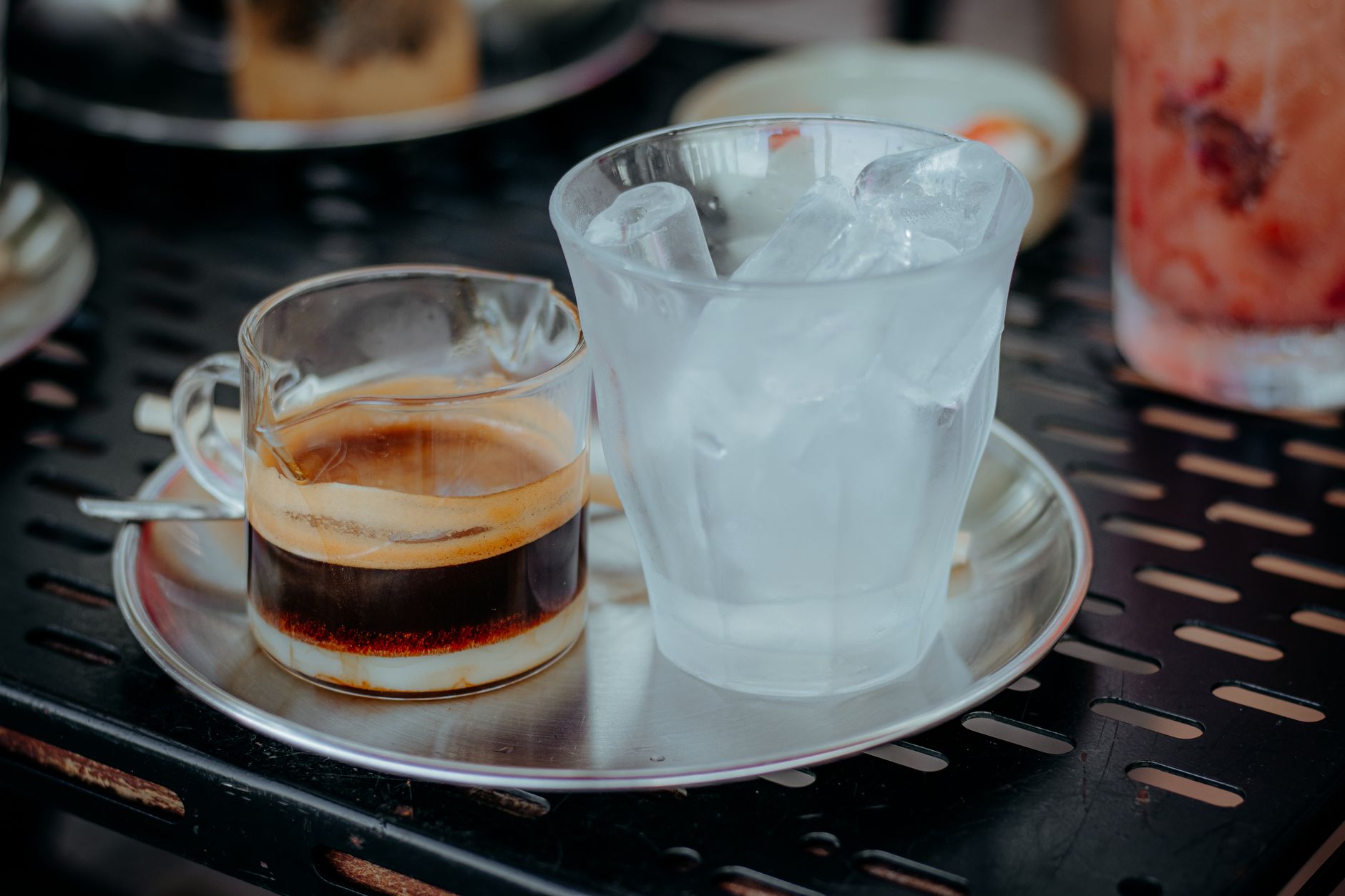 Close-up of an iced Americano showing layered espresso and ice glass on a metal tray.