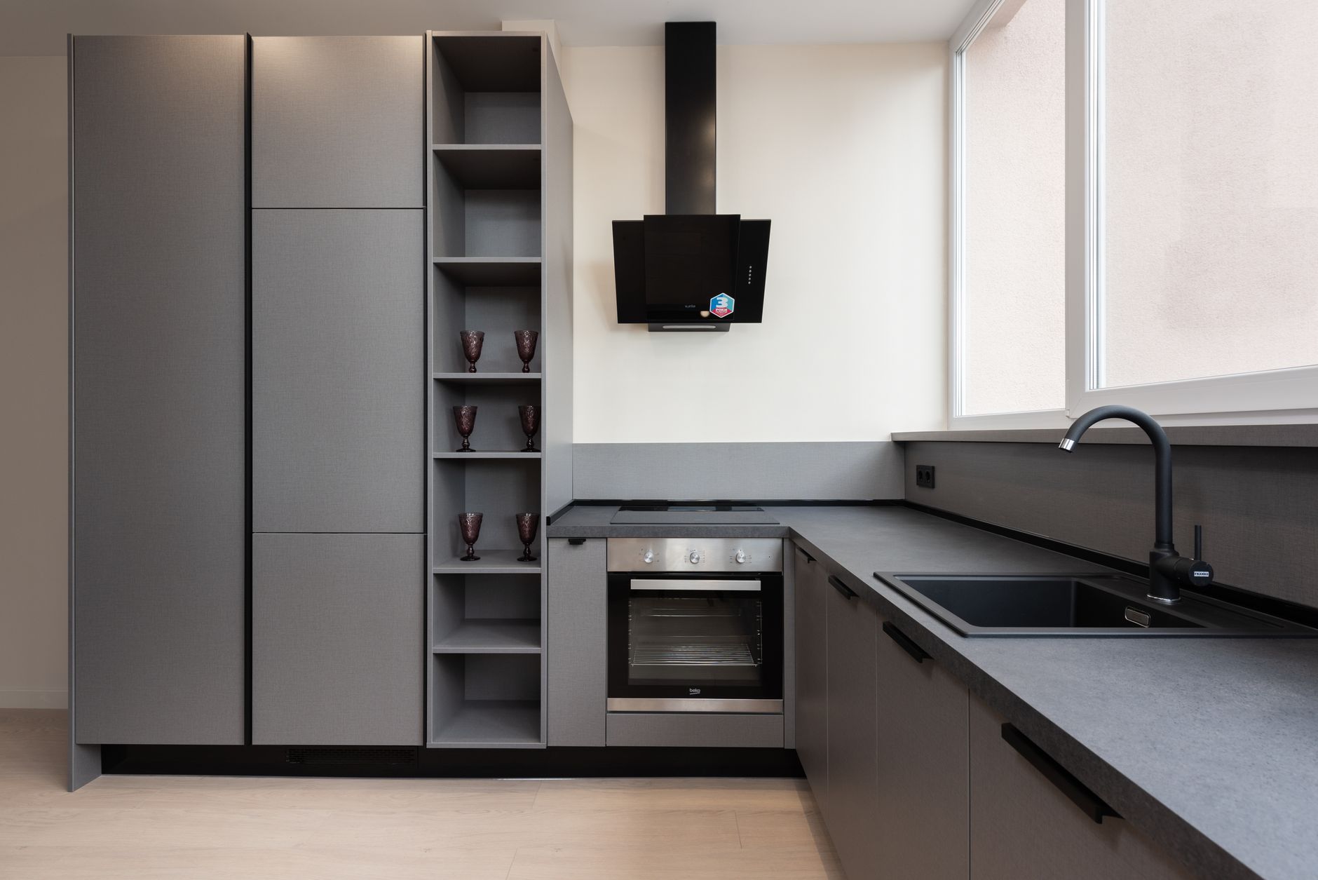 Interior of light gray kitchen corner furnished with cupboards and stone counter with built in oven and sink placed with big windows in apar