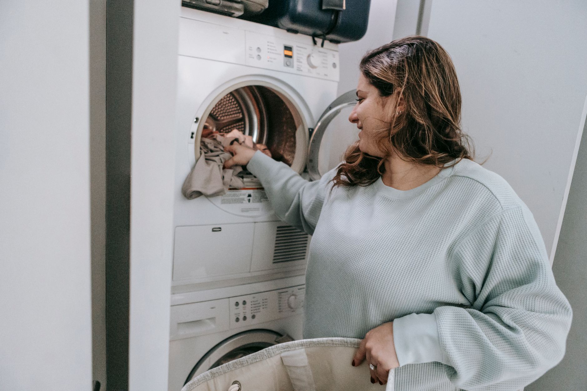 Glad female in casual wear loading dirt clothes in modern white washing machine while sitting in bathroom during household routine