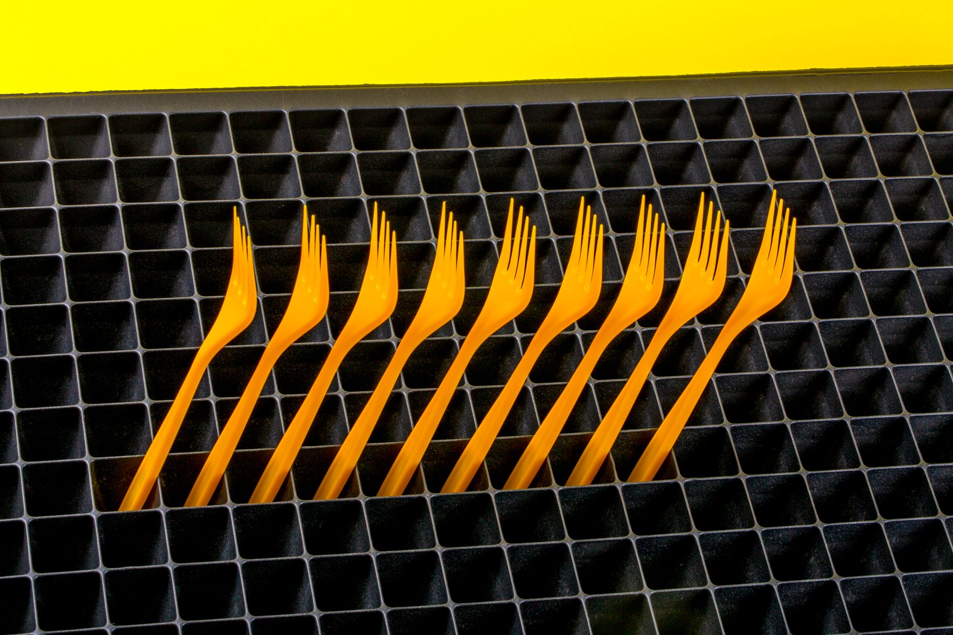 Bright orange plastic forks arranged neatly on a dark grid pattern background.