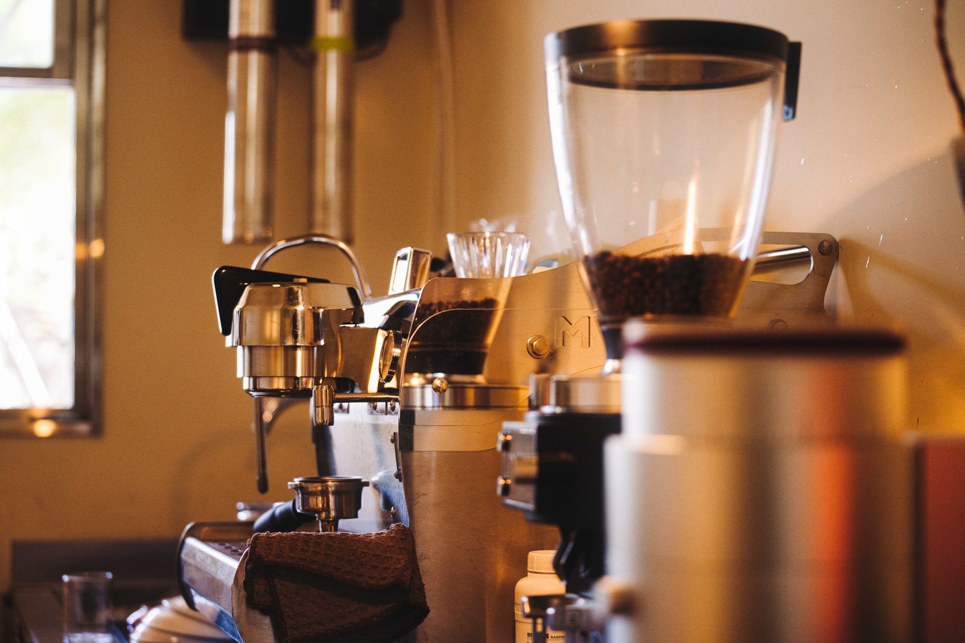 A modern espresso machine and coffee grinder in a cozy indoor coffee shop setting with warm lighting.